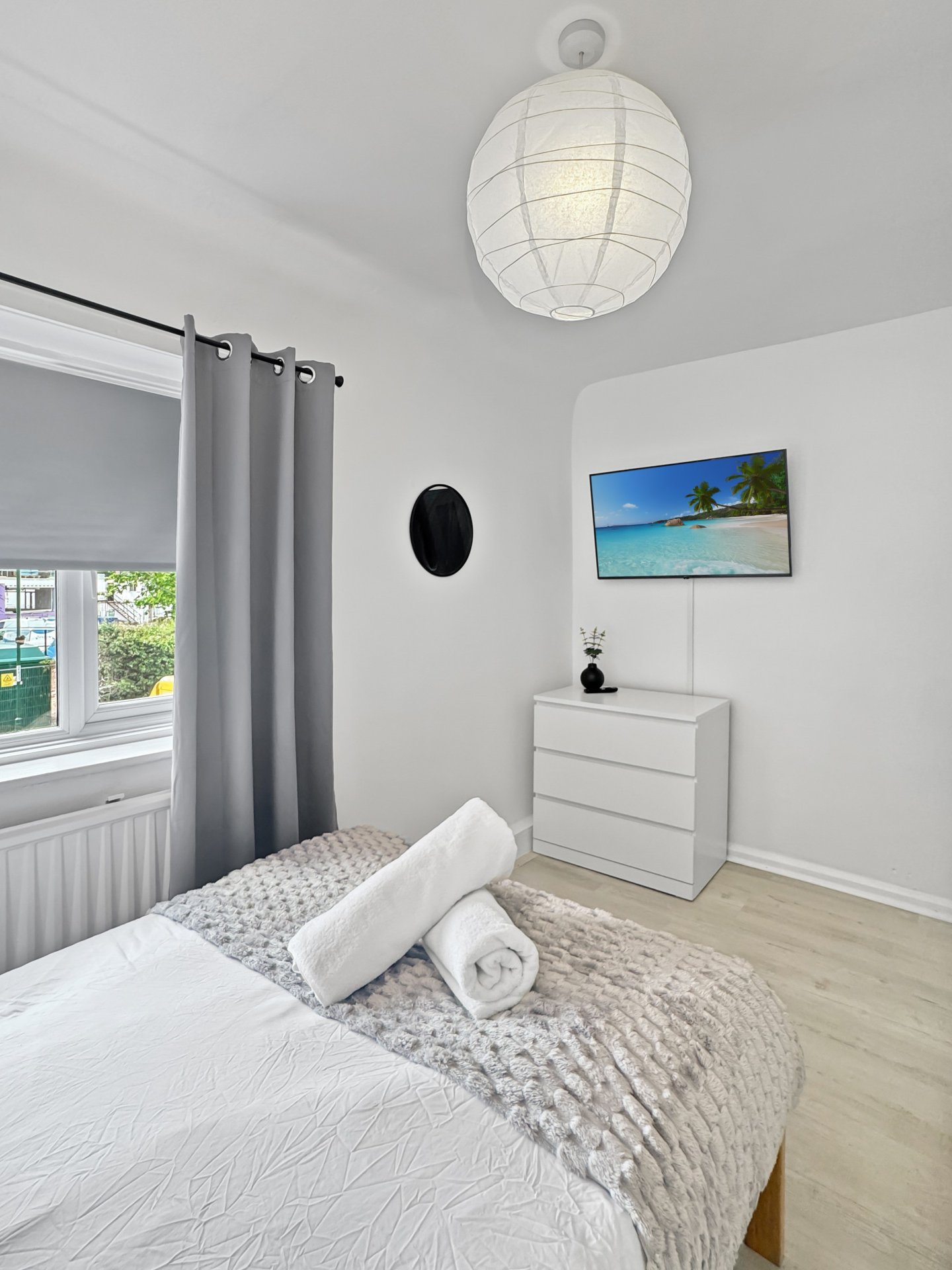 Bright bedroom with double bed, white bedding, wooden dresser, pendant light and window