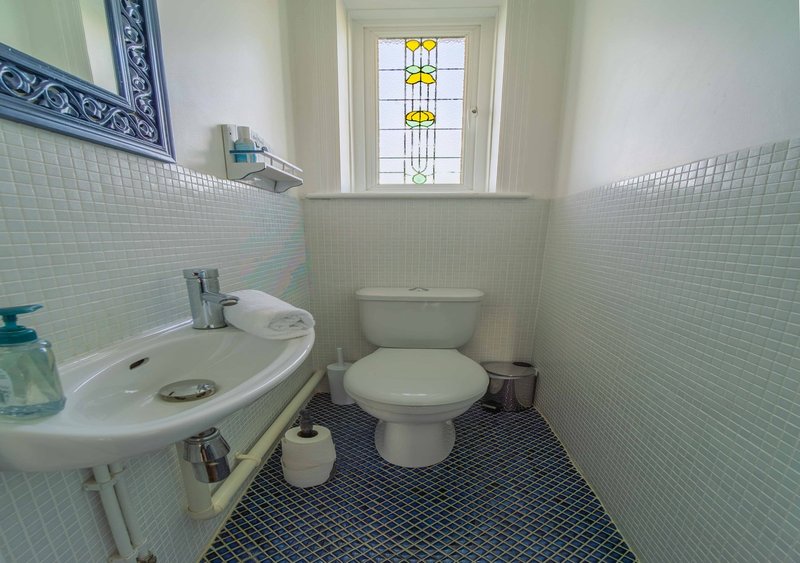 Small bathroom with pedestal sink, toilet, pale green tile walls and dark tile floor