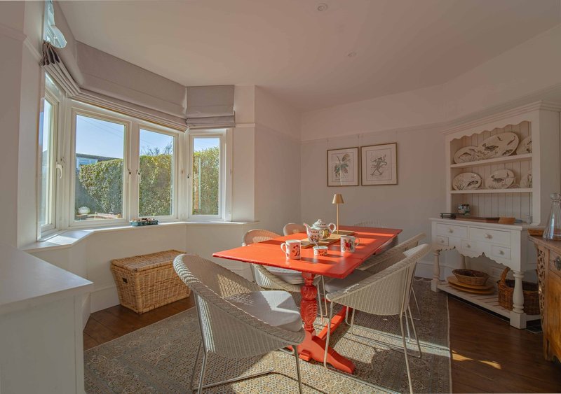 Bright dining room with red table, wicker chairs, bay windows and garden views
