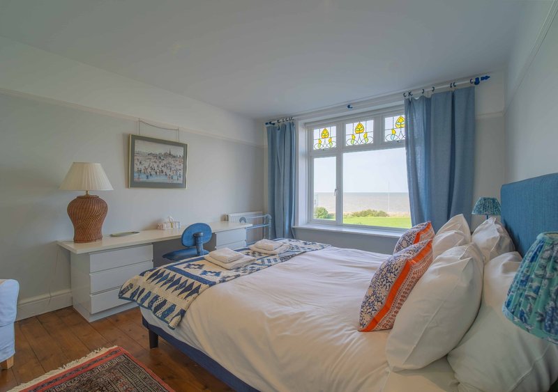 Bright bedroom with double bed, desk, wooden floor and sea view from large windows