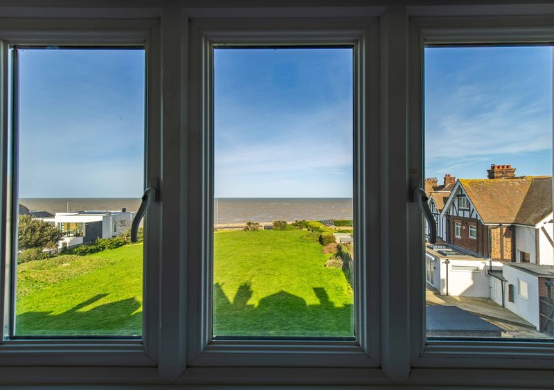 View through triple-pane windows showing green fields, distant buildings and coastal landscape