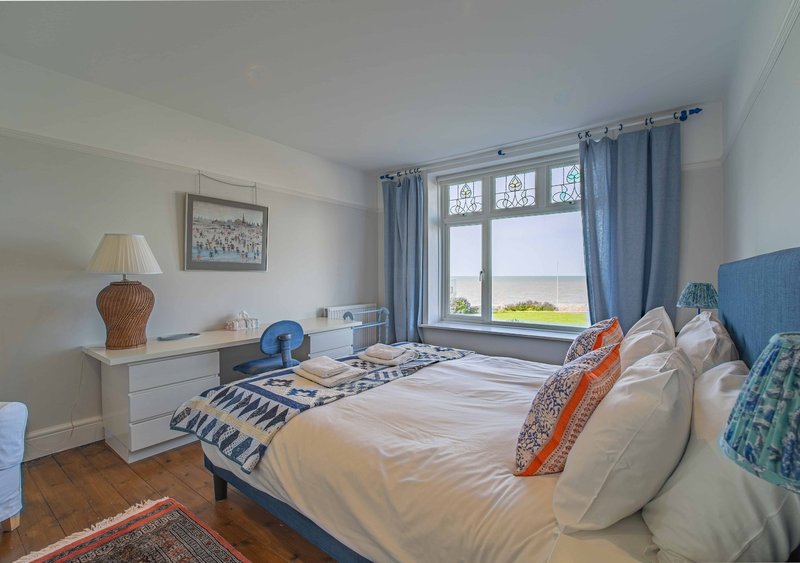 Bright bedroom with double bed, blue headboard, desk, lamp and sea view from windows