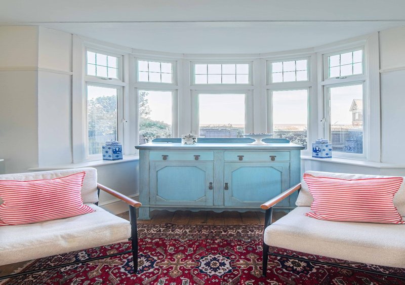 Bright bay window seating area with turquoise cabinet, pink striped cushions and city views