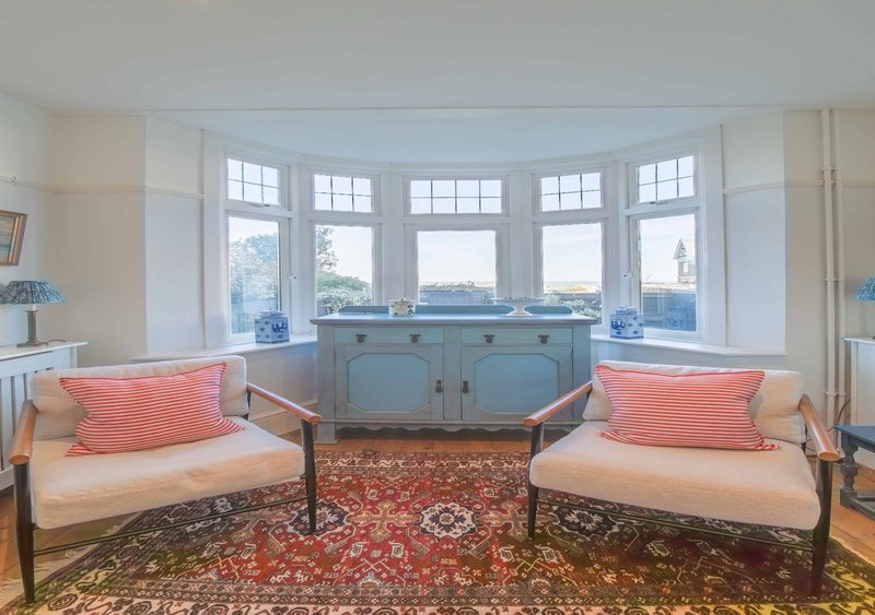 Bright sunroom with bay windows, two upholstered chairs, coral cushions, and patterned rug
