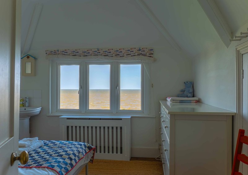 Bright bedroom with single bed, radiator, triple-glazed windows overlooking fields, and wooden flooring