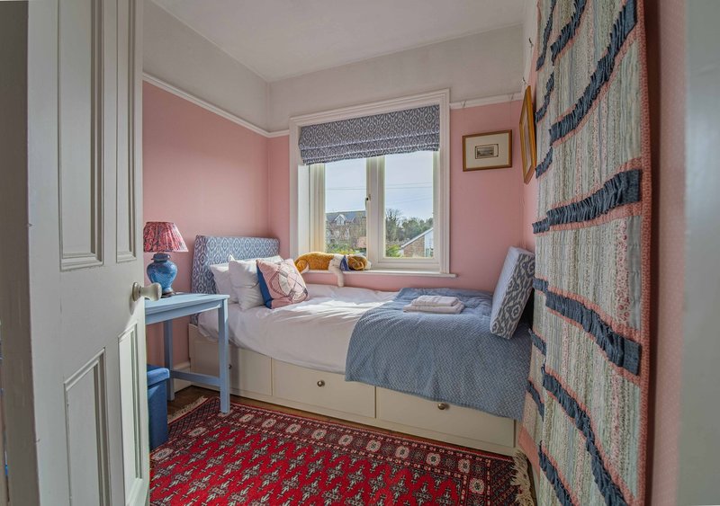 Bedroom with pink walls, single bed, desk, window with countryside view