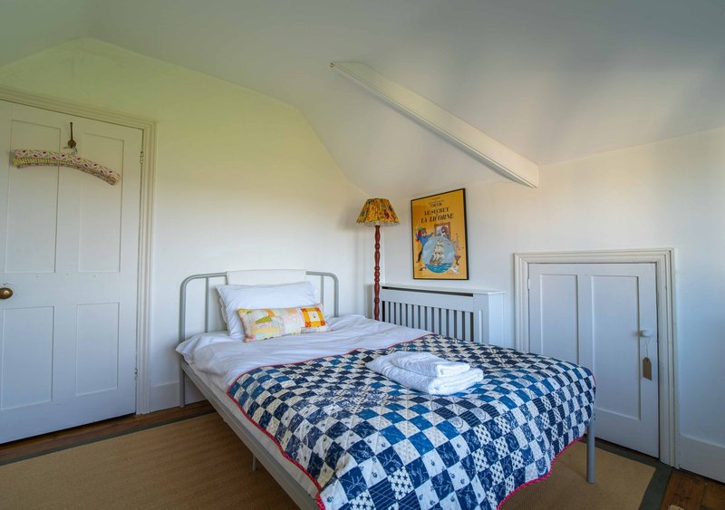 Bright attic bedroom with metal bed frame, blue checkered quilt, wooden floor and white doors