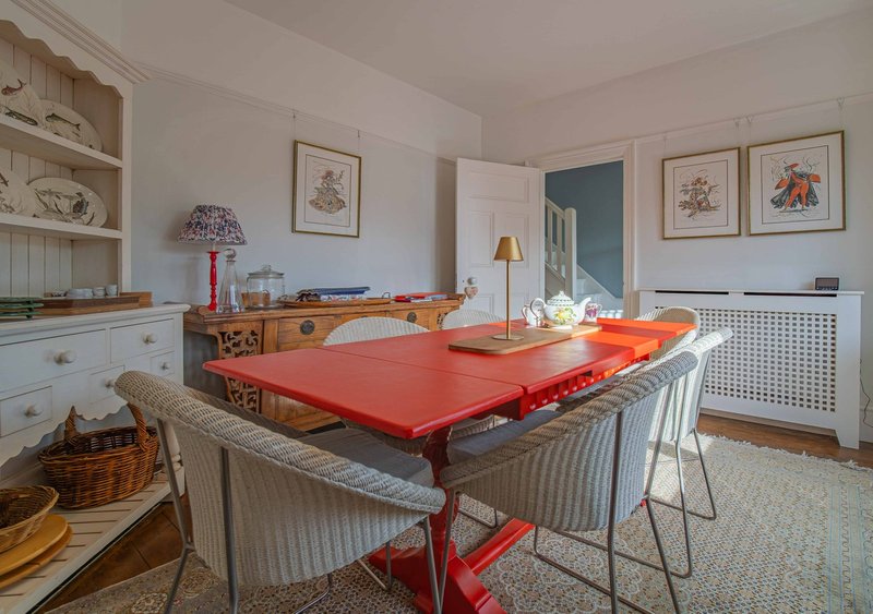 Bright kitchen-dining area with red table, upholstered chairs, open shelving and framed botanical prints