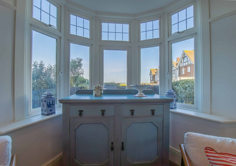 Bay window with gray cabinet, blue cushions, and exterior views of garden and neighboring houses