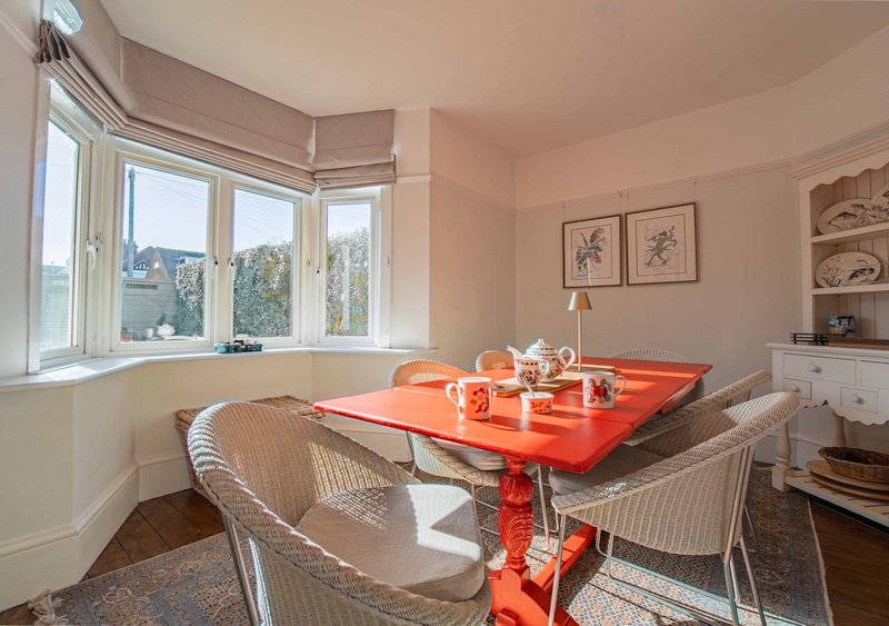 Bright dining room with red table, wicker chairs, bay windows and framed botanical prints