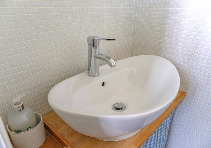 Modern bathroom with oval white sink, chrome faucet, wooden countertop and tile walls