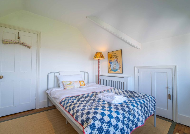 Bright attic bedroom with single metal bed, blue checkered quilt, and sloped ceiling