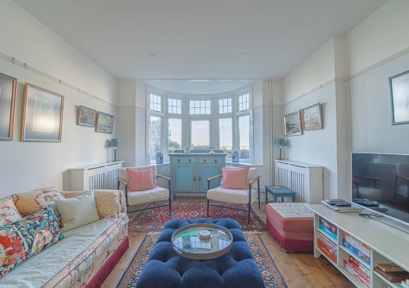 Bright living room with bay window, two sofas, round blue ottoman and TV on wooden floor
