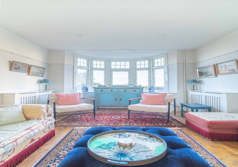 Bright children's bedroom with twin beds, bay window, central blue circular play mat and pink seating