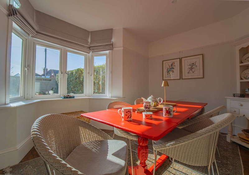 Bright dining area with red table, wicker chairs, large windows and city views