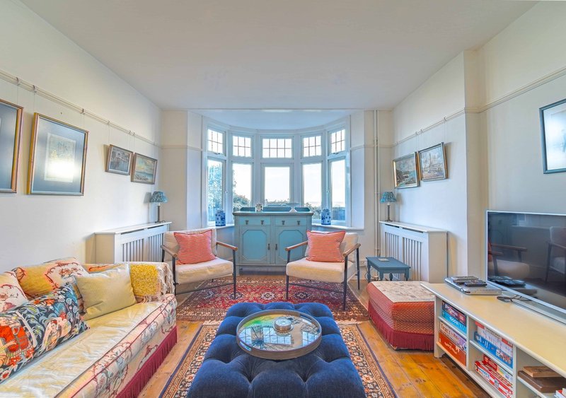Bright living room with bay window, colorful seating, patterned rug and fireplace