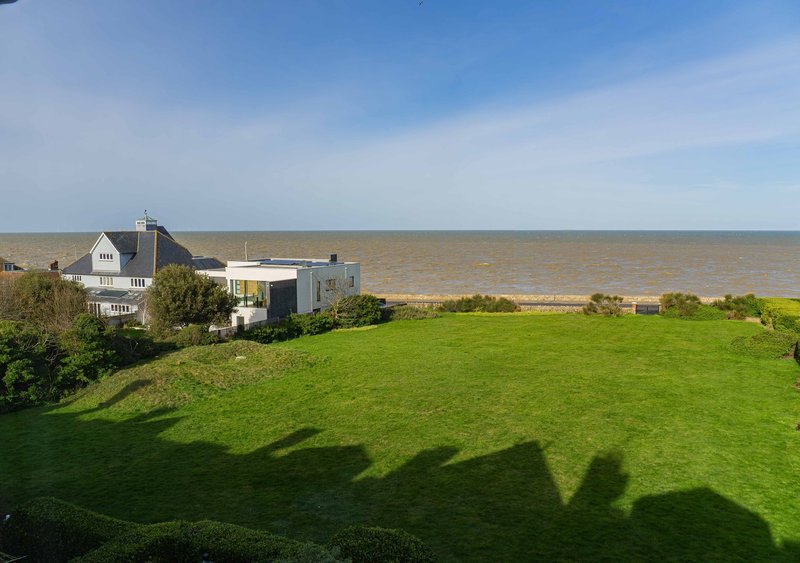 Coastal property with white house, green lawn and sea view in background