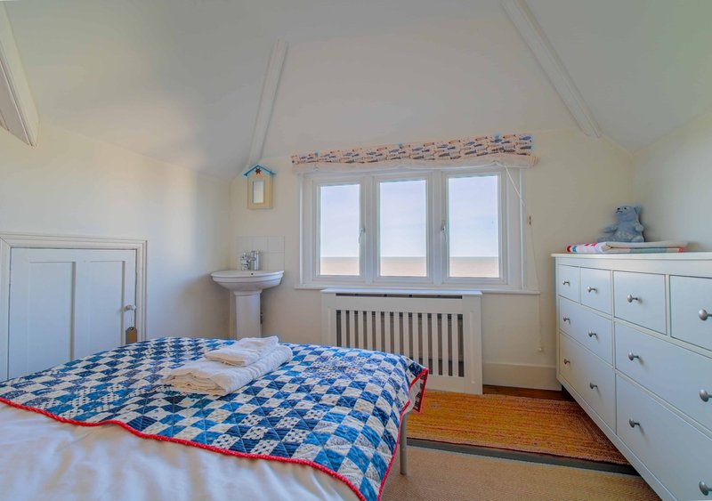 Bright bedroom with double bed, blue geometric quilt, white furniture and sea view through windows