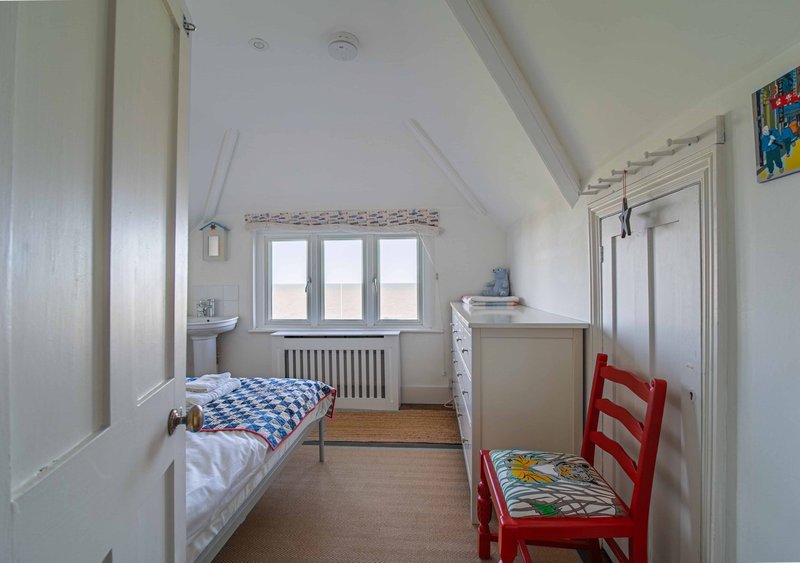 Bright children's bedroom with two single beds, red chair, and wooden flooring