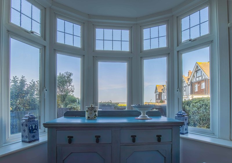 Bay window with blue-painted cabinet, decorative items, and views of gardens and buildings outside