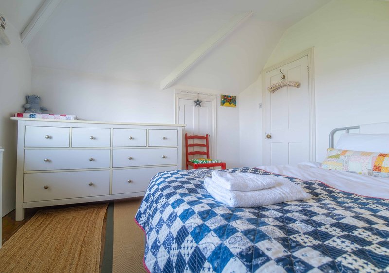 Bright attic bedroom with sloped ceiling, white dresser, blue patterned bedding, wooden floor
