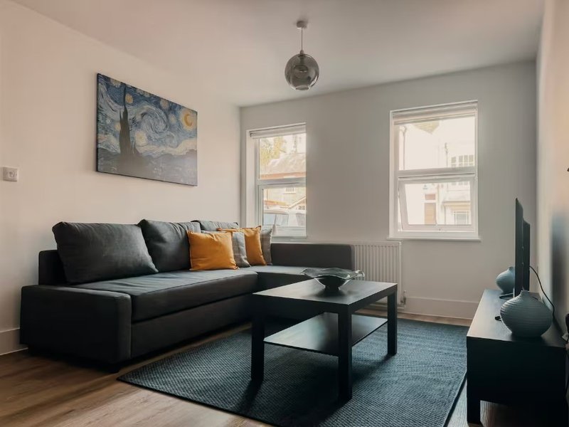 Modern living room with black sofa, coffee table, blue area rug, and framed wall art
