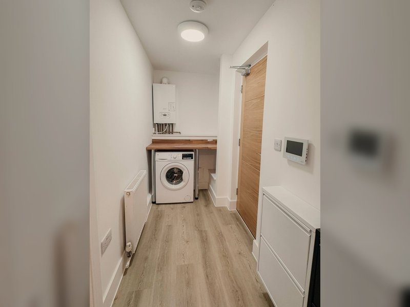 Utility room with washing machine, wooden countertop, boiler, and wooden flooring