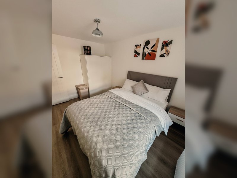 Compact bedroom with double bed, grey headboard, wooden floor and wall art