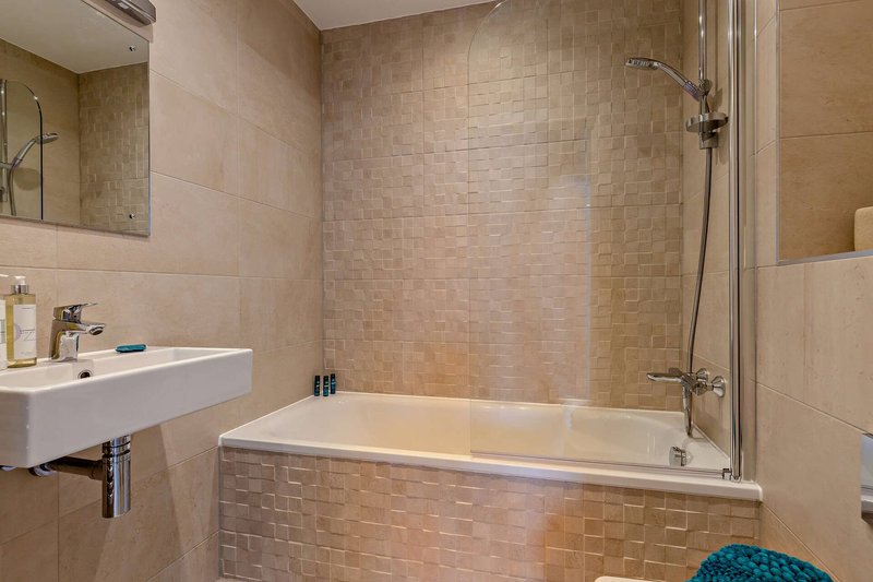 Modern bathroom with white sink, bathtub, glass shower screen and tiled walls