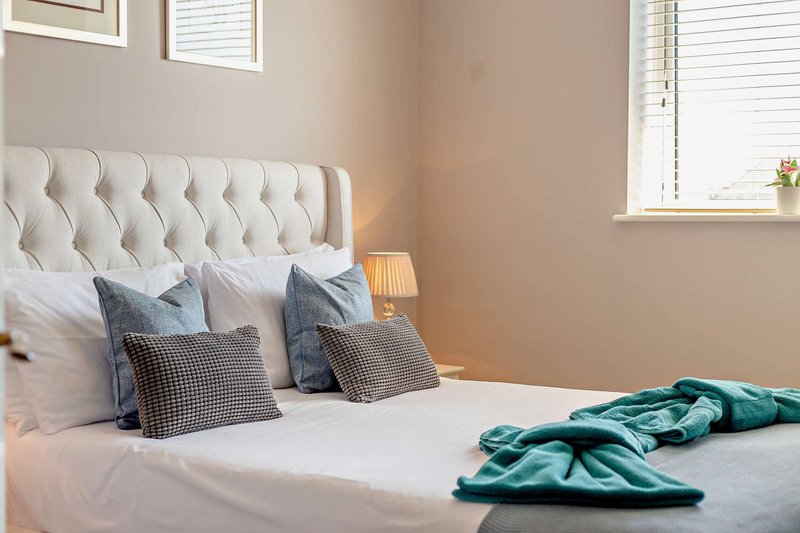 Bedroom with upholstered headboard, white bedding, decorative pillows and folded teal blankets