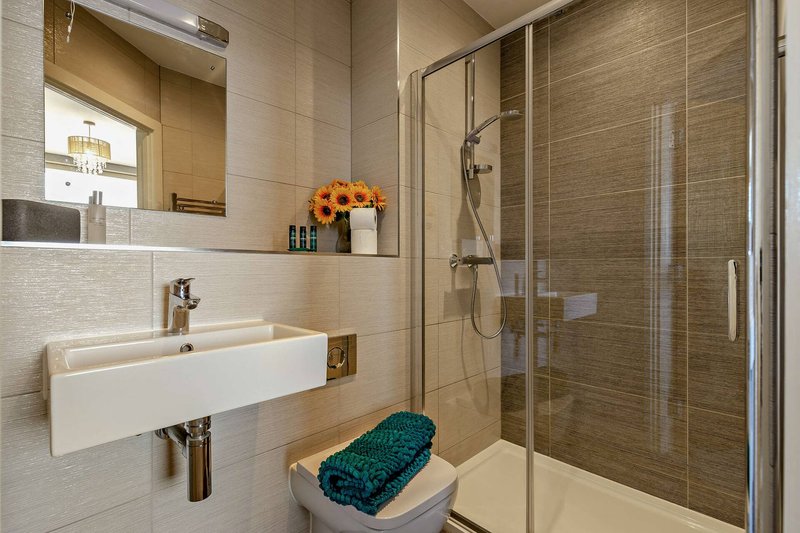 Modern bathroom with wall-mounted sink, glass shower enclosure, and teal bath mat