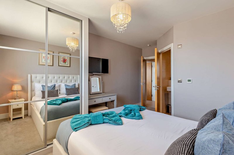 Modern bedroom with double bed, turquoise throws, mirrored wardrobe and crystal pendant lights