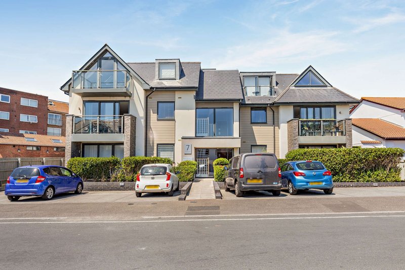 Modern multi-unit residential building with parked cars on street frontage and blue sky
