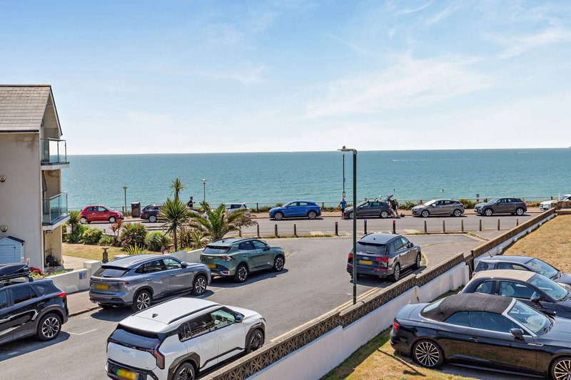 Coastal property with sea view, parking area, and parked vehicles visible