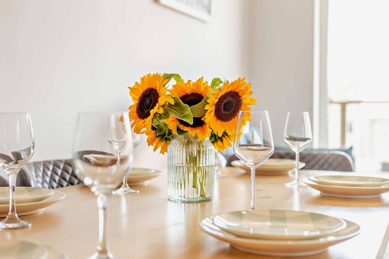 Dining table set with place settings, glasses, and sunflower centerpiece arrangement