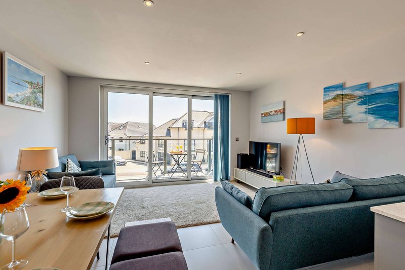 Modern open-plan living room with dining table, grey sofa, and balcony overlooking residential street