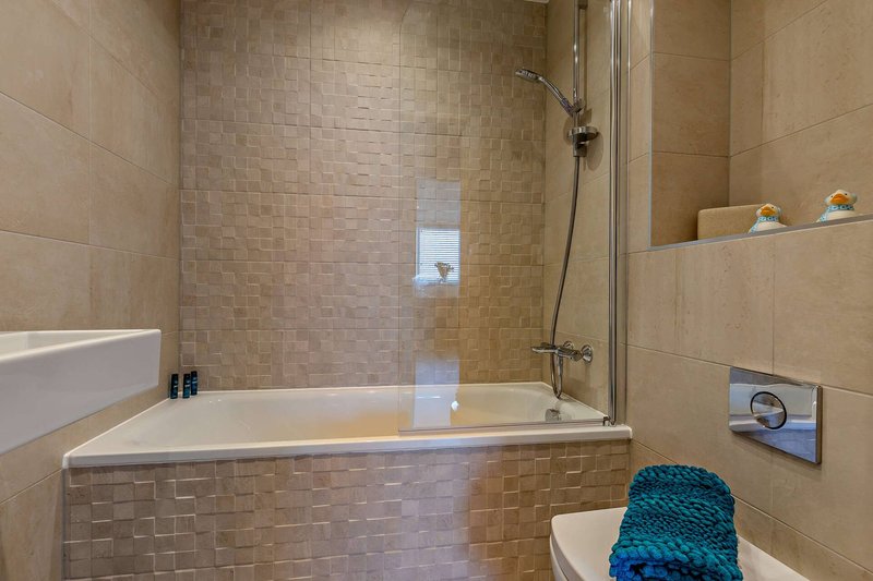 Modern bathroom with built-in bathtub, glass shower screen, tiled walls and shelving