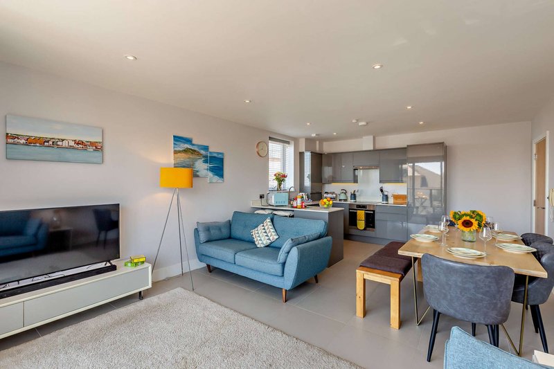 Open-plan living room with blue sofa, dining table, TV unit and kitchen area visible beyond