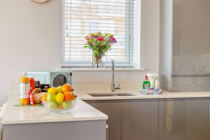 Modern kitchen with white countertop, fresh flowers, fruit bowl, and cleaning supplies