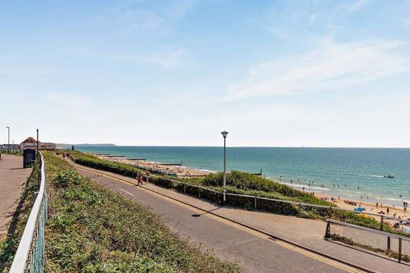 Coastal promenade with grassy slope, beach, sea, and clear blue sky