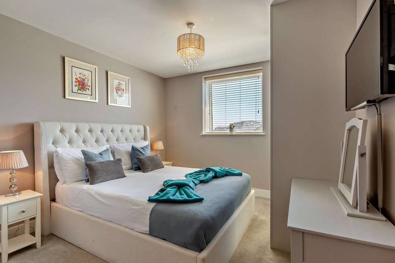 Modern bedroom with white upholstered headboard, double bed, teal throw, pendant light and bedside tables