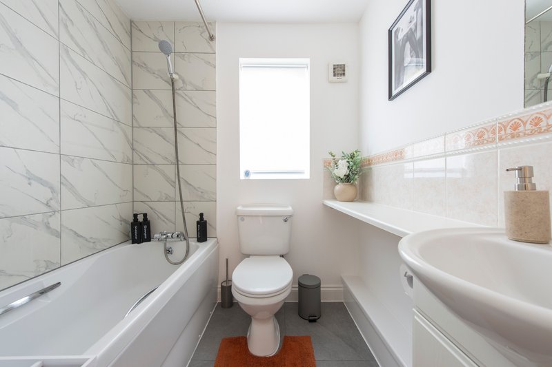 Modern bathroom with white tile walls, bathtub, toilet, pedestal sink and window