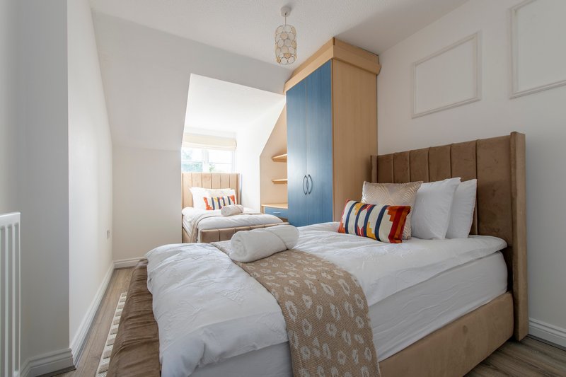Bright bedroom with double bed, brown upholstered headboard, and view into adjacent room