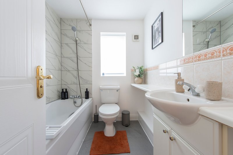 Modern bathroom with bathtub, toilet, pedestal sink, marble tiles and natural light