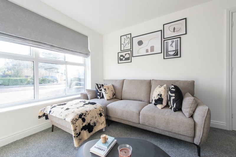 Modern living room with grey corner sofa, cow-print footstool, and framed wall art