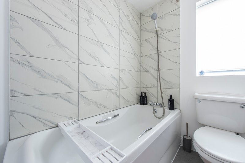 Modern bathroom with marble-effect tile walls, white bathtub, and toilet