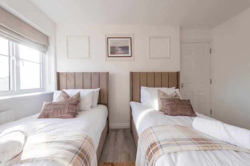 Twin bedroom with two beds, neutral headboards, white bedding and plaid throws
