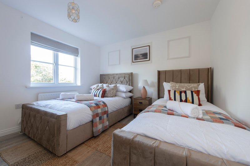 Bright twin bedroom with two upholstered beds, wooden floor, and large window
