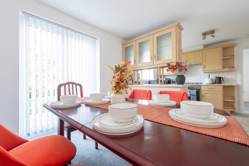 Open-plan kitchen and dining area with wooden cabinets, dining table set with plates and orange accents