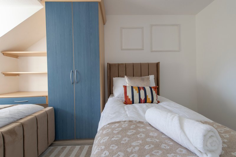 Bedroom with single bed, blue wardrobe, wooden shelving and striped cushion